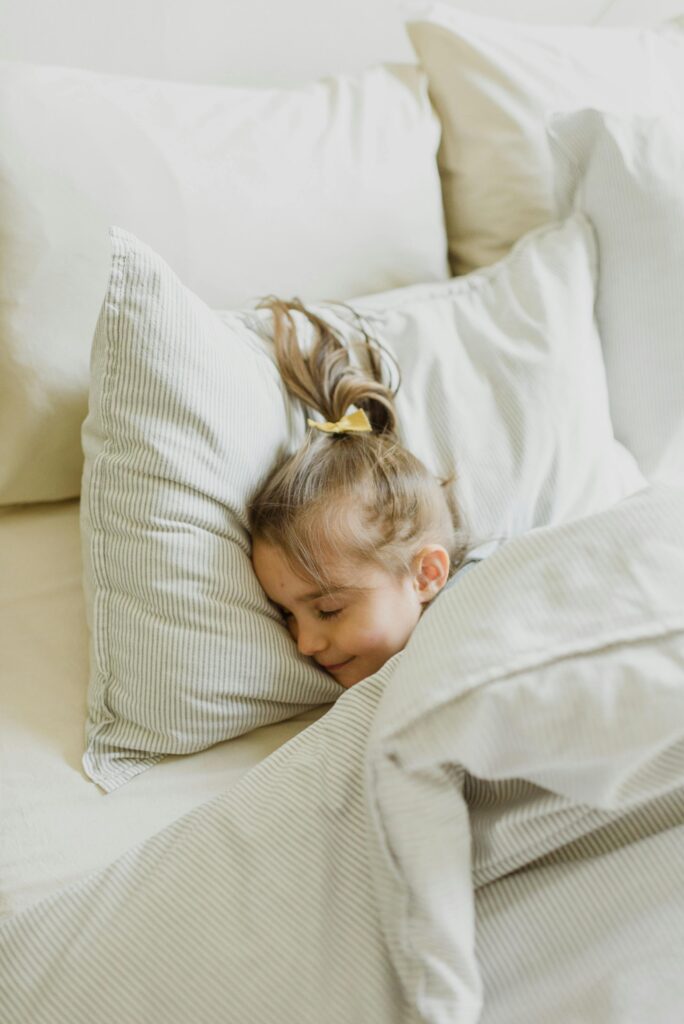 A peacefully sleeping child nestled in white pillows and a warm blanket.